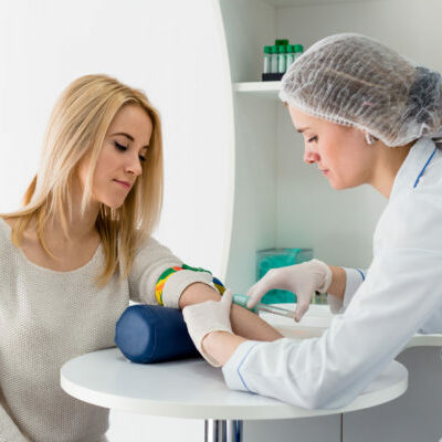 42628725 - blood test from vein with beautiful young blond woman by female doctor in white coat medical uniform on the table in white bright room.